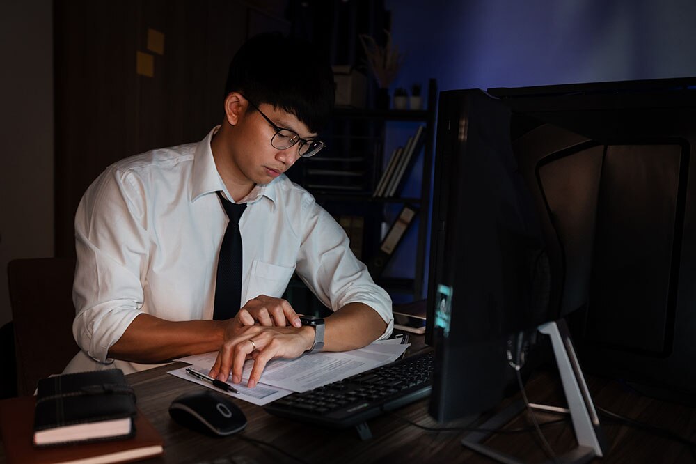 時計を確認しながら残業中のサラリーマン